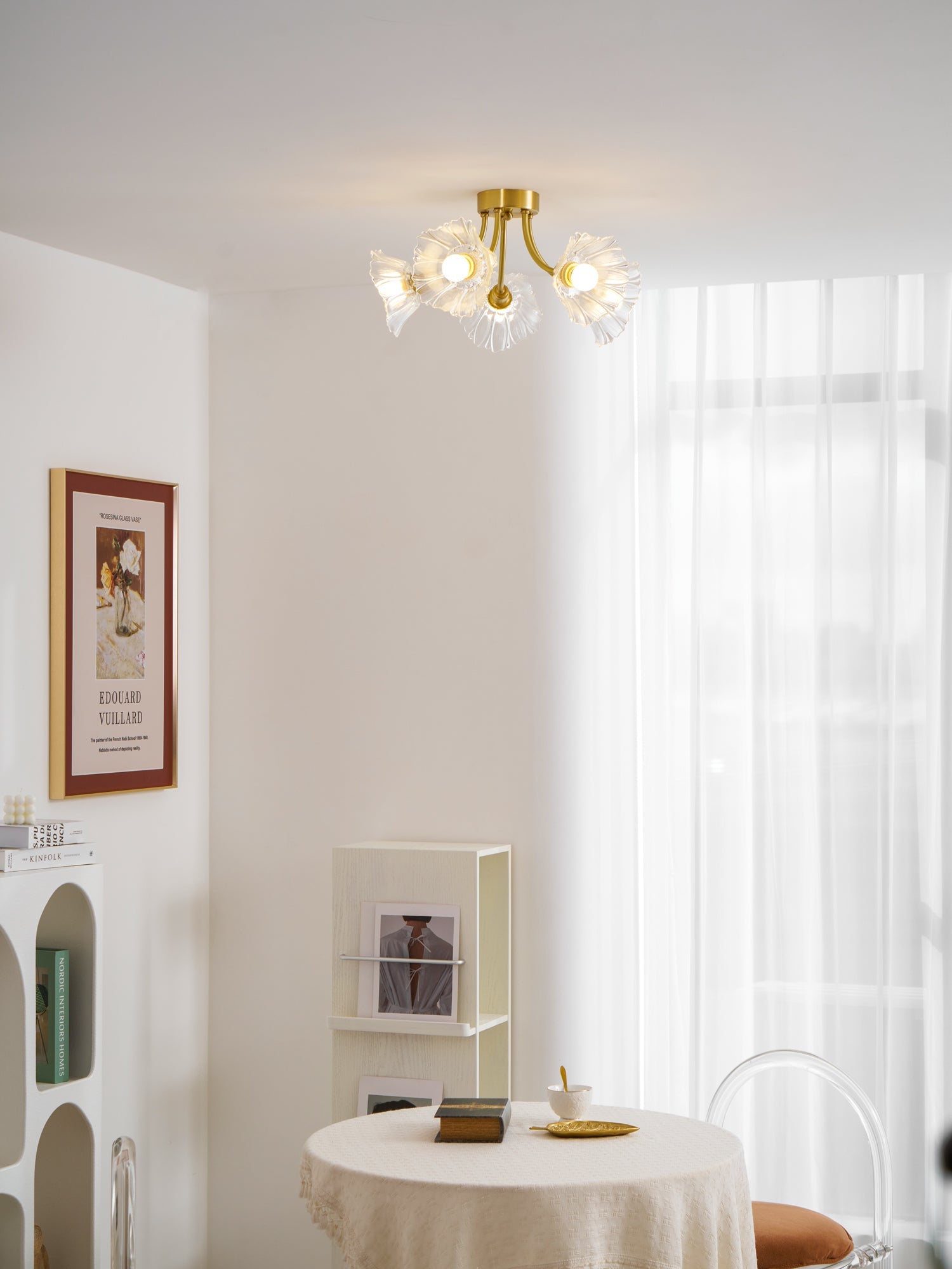 Flush-mount ceiling lamp with curved brass arms holding clear ribbed flower-shaped glass shades lit on a ceiling above a round table.
