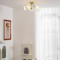 Flush-mount ceiling lamp with curved brass arms holding clear ribbed flower-shaped glass shades lit on a ceiling above a round table.