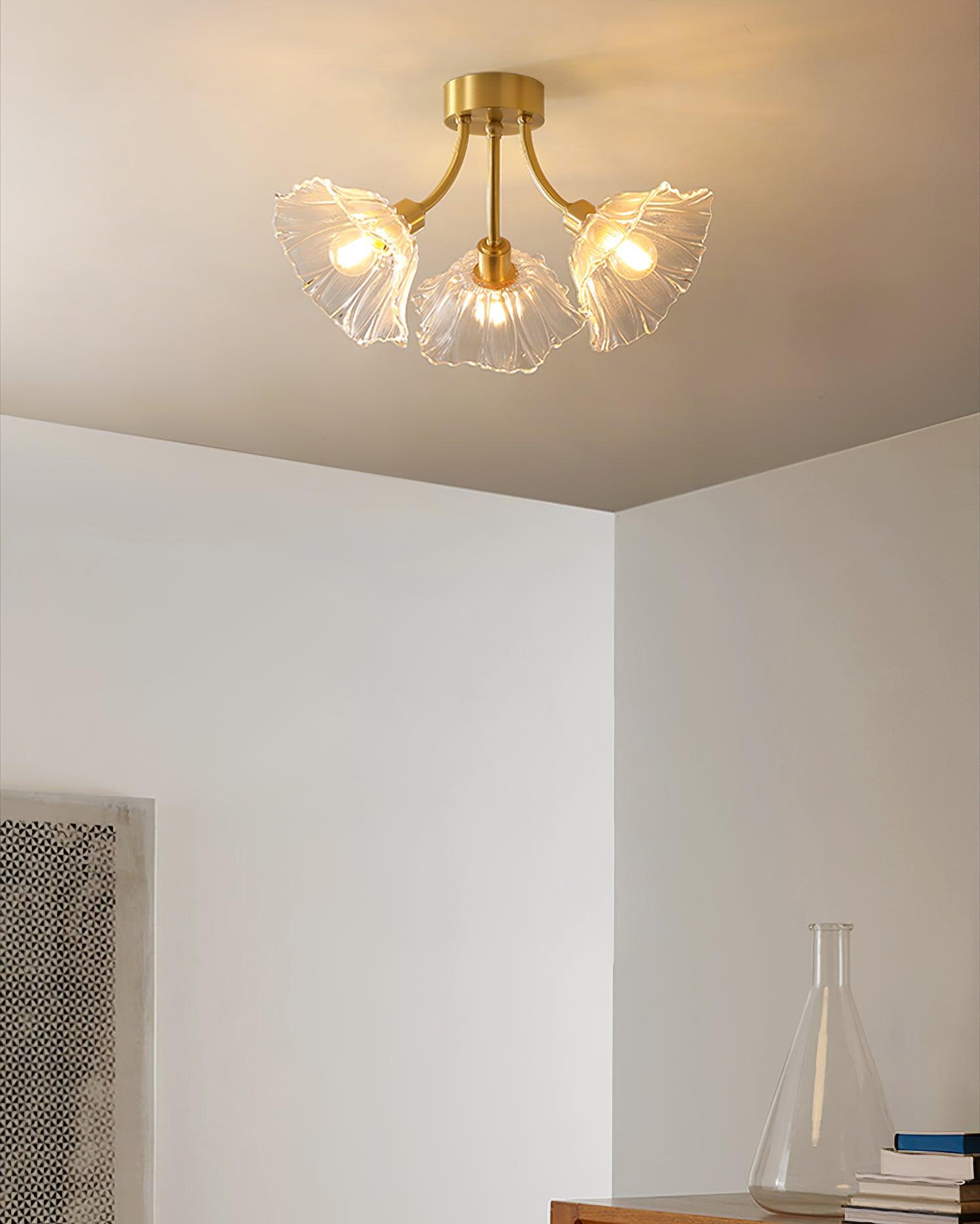 Flush-mount ceiling lamp with curved brass arms holding clear ribbed flower-shaped glass shades lit on a ceiling in a corner of a room.