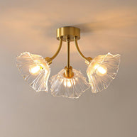 Flush-mount ceiling lamp with curved gold-toned arms holding clear ribbed flower-shaped glass shades, lit, seen from below against a warm wall.