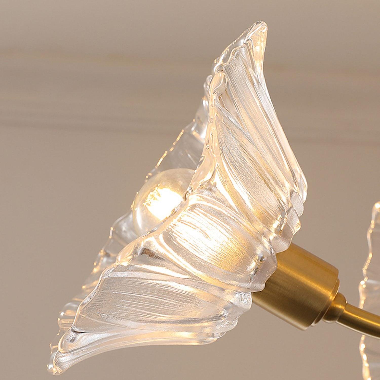 Close view of one clear flower-shaped glass shade on its brass arm.