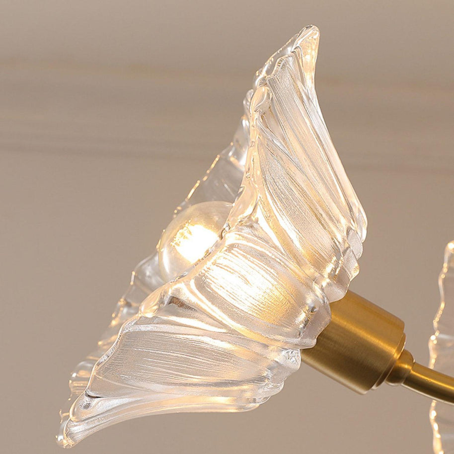 Close view of one clear flower-shaped glass shade on its brass arm.
