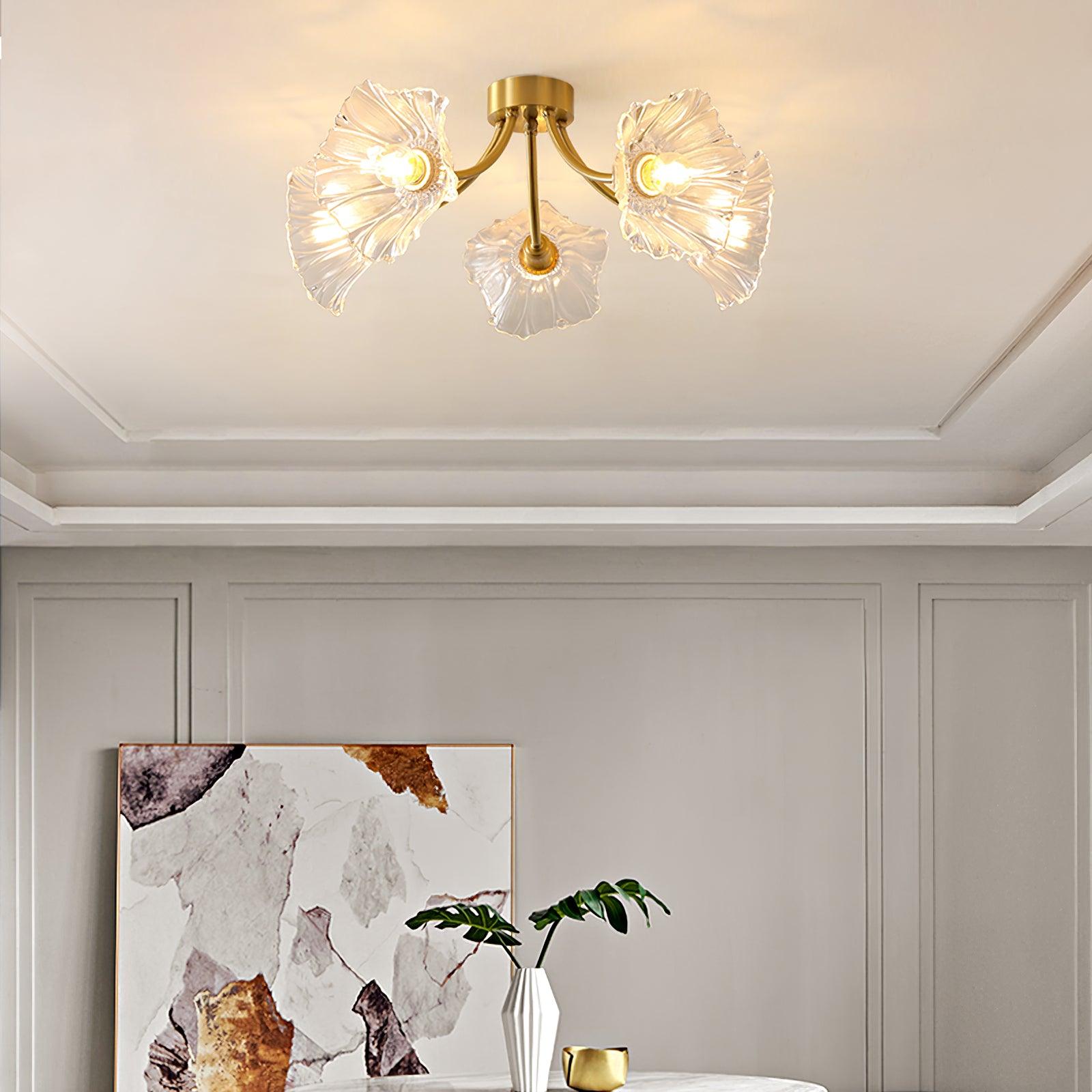 Flush-mount ceiling lamp with curved brass arms holding clear ribbed flower-shaped glass shades lit on a ceiling above framed artwork.