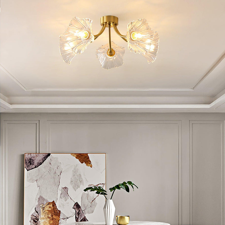 Flush-mount ceiling lamp with curved brass arms holding clear ribbed flower-shaped glass shades lit on a ceiling above framed artwork.