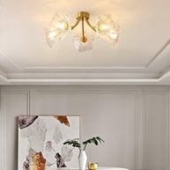 Flush-mount ceiling lamp with curved brass arms holding clear ribbed flower-shaped glass shades lit on a ceiling above framed artwork.