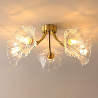 Flush-mount ceiling lamp with curved brass arms holding clear ribbed flower-shaped glass shades, lit, seen close on a ceiling.