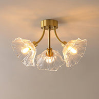 Flush-mount ceiling lamp with curved gold-toned arms holding clear ribbed flower-shaped glass shades, lit, seen from below and slightly to one side.