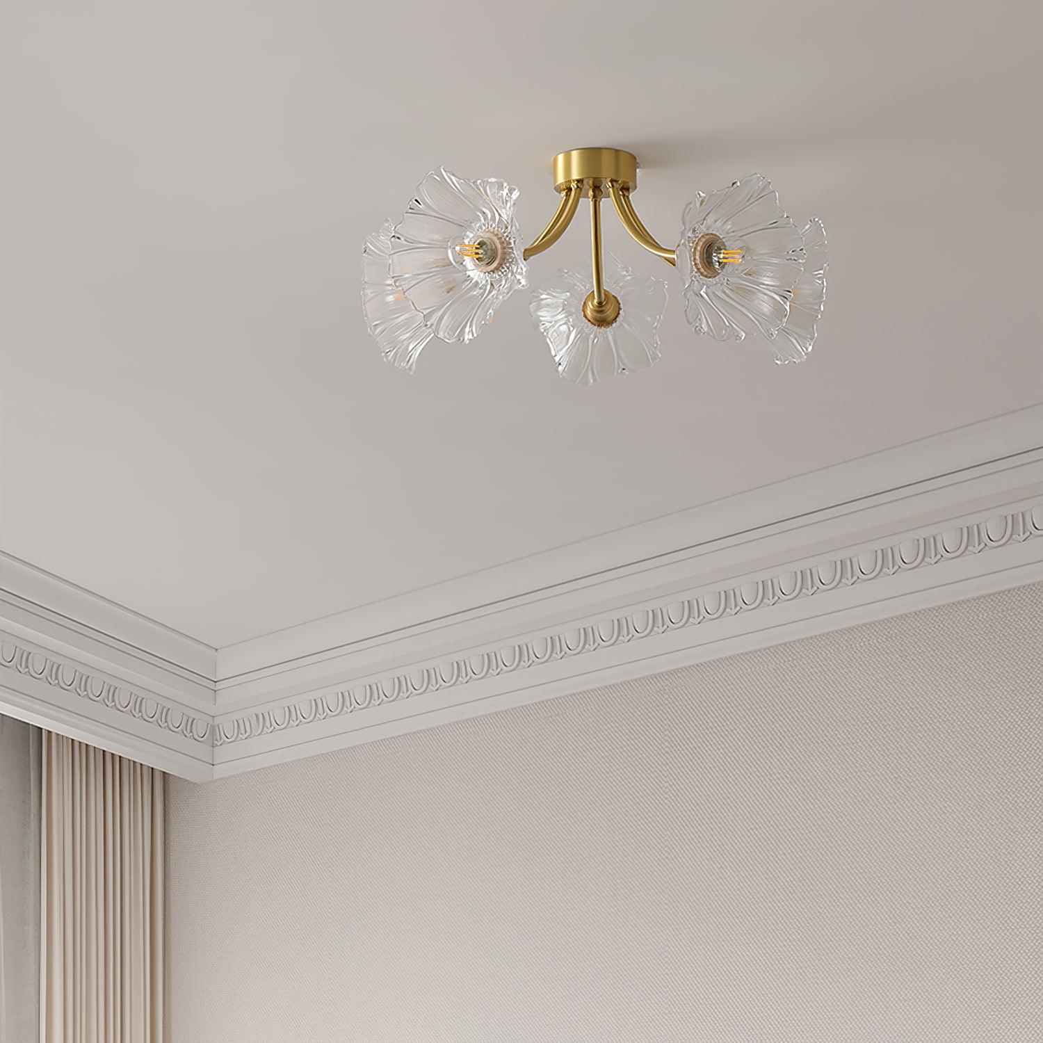 Flush-mount ceiling lamp with curved brass arms holding clear ribbed flower-shaped glass shades on a ceiling beside a moulded cornice.