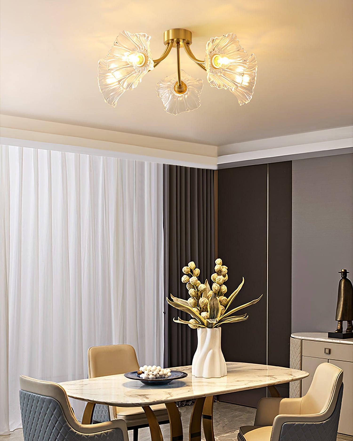 Flush-mount ceiling lamp with curved brass arms holding clear ribbed flower-shaped glass shades lit above a dining table.