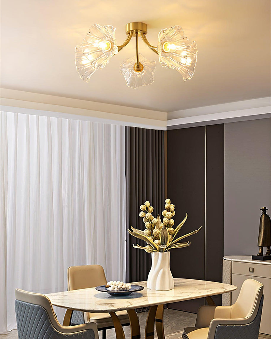 Flush-mount ceiling lamp with curved brass arms holding clear ribbed flower-shaped glass shades lit above a dining table.