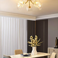 Flush-mount ceiling lamp with curved brass arms holding clear ribbed flower-shaped glass shades lit above a dining table.