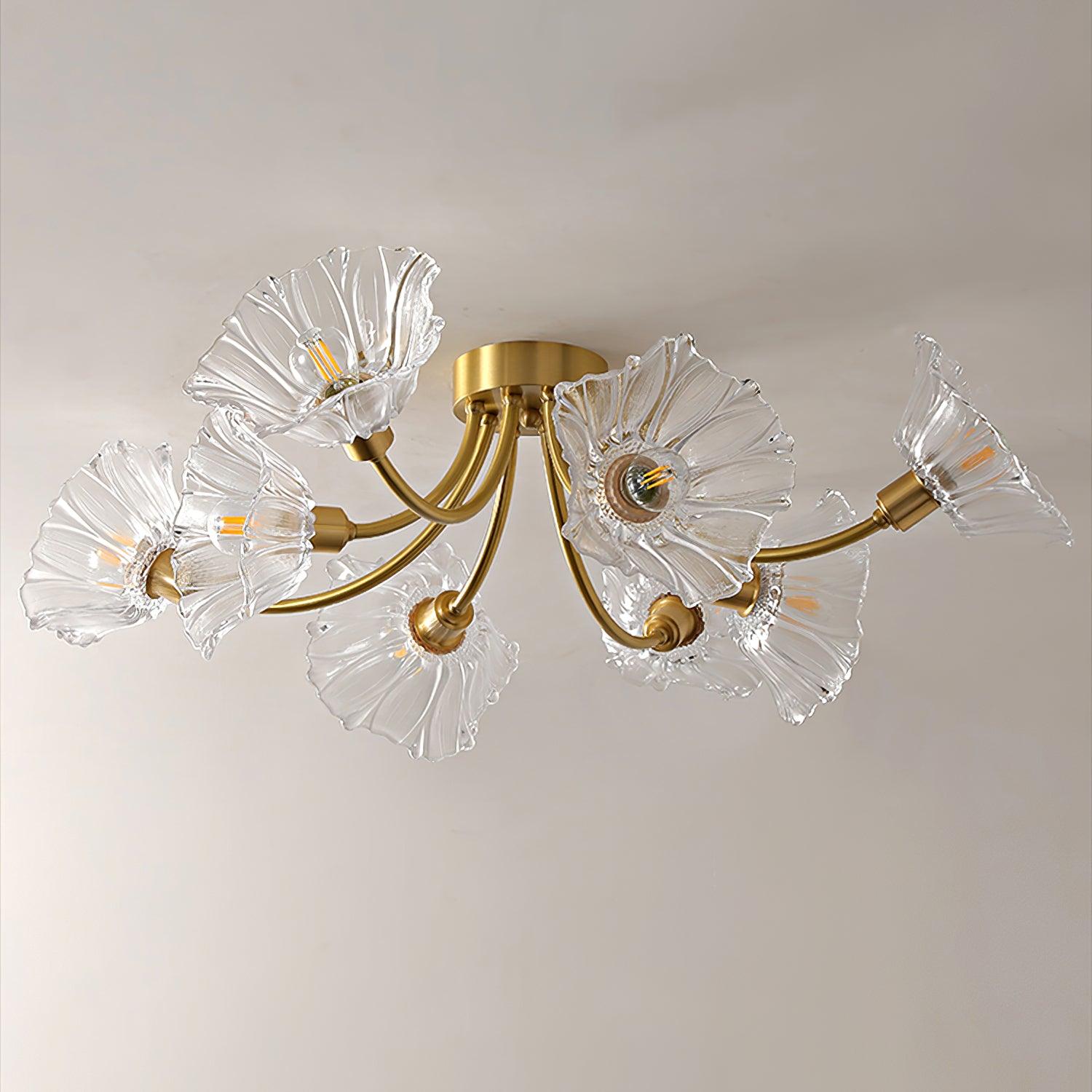 Flush-mount ceiling lamp with curved brass arms holding clear ribbed flower-shaped glass shades, lit, seen close from below.