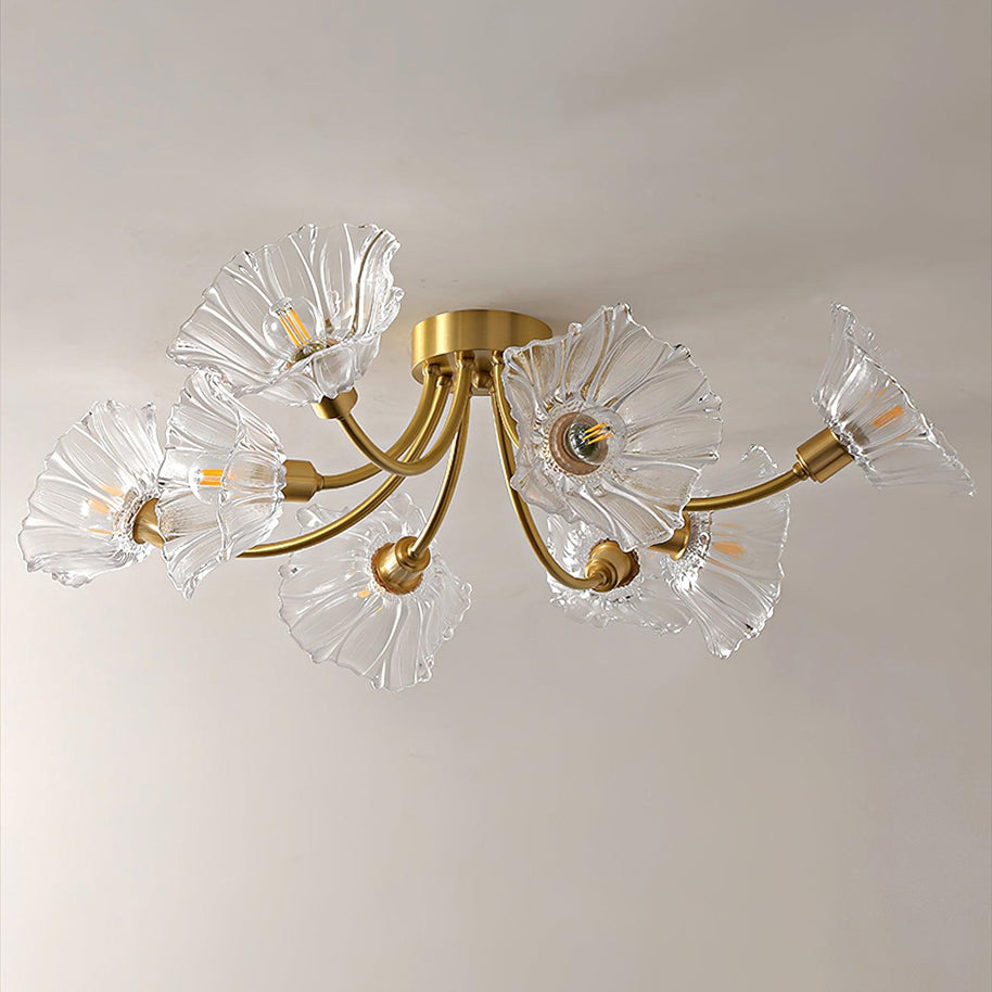 Flush-mount ceiling lamp with curved brass arms holding clear ribbed flower-shaped glass shades, lit, seen close from below.