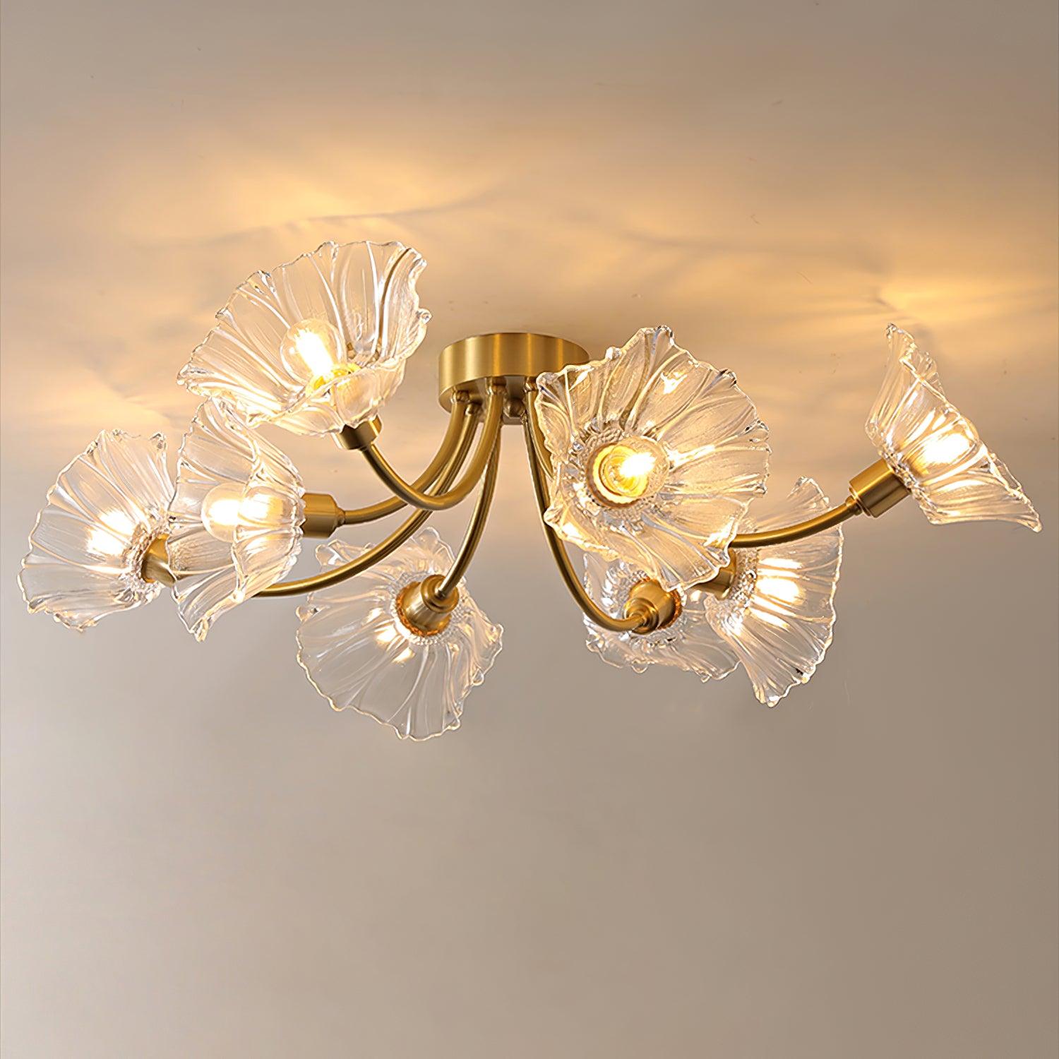 Flush-mount ceiling lamp with curved brass arms holding clear ribbed flower-shaped glass shades, lit, with the arms spread wide across the ceiling.