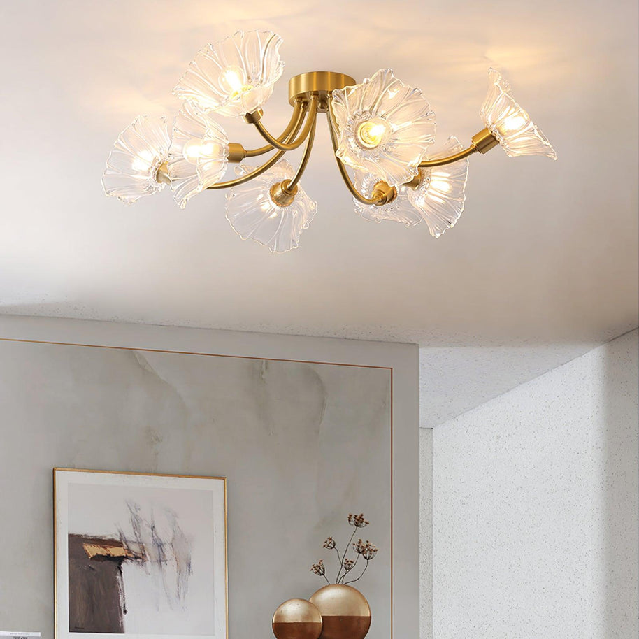 Flush-mount ceiling lamp with curved brass arms holding clear ribbed flower-shaped glass shades lit on a ceiling above a framed picture.