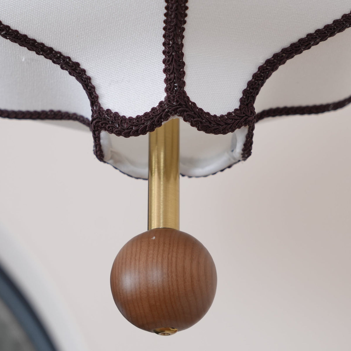 Macro of the shade hem: woven brown braid on white fabric, brass rod and a turned wooden bead.