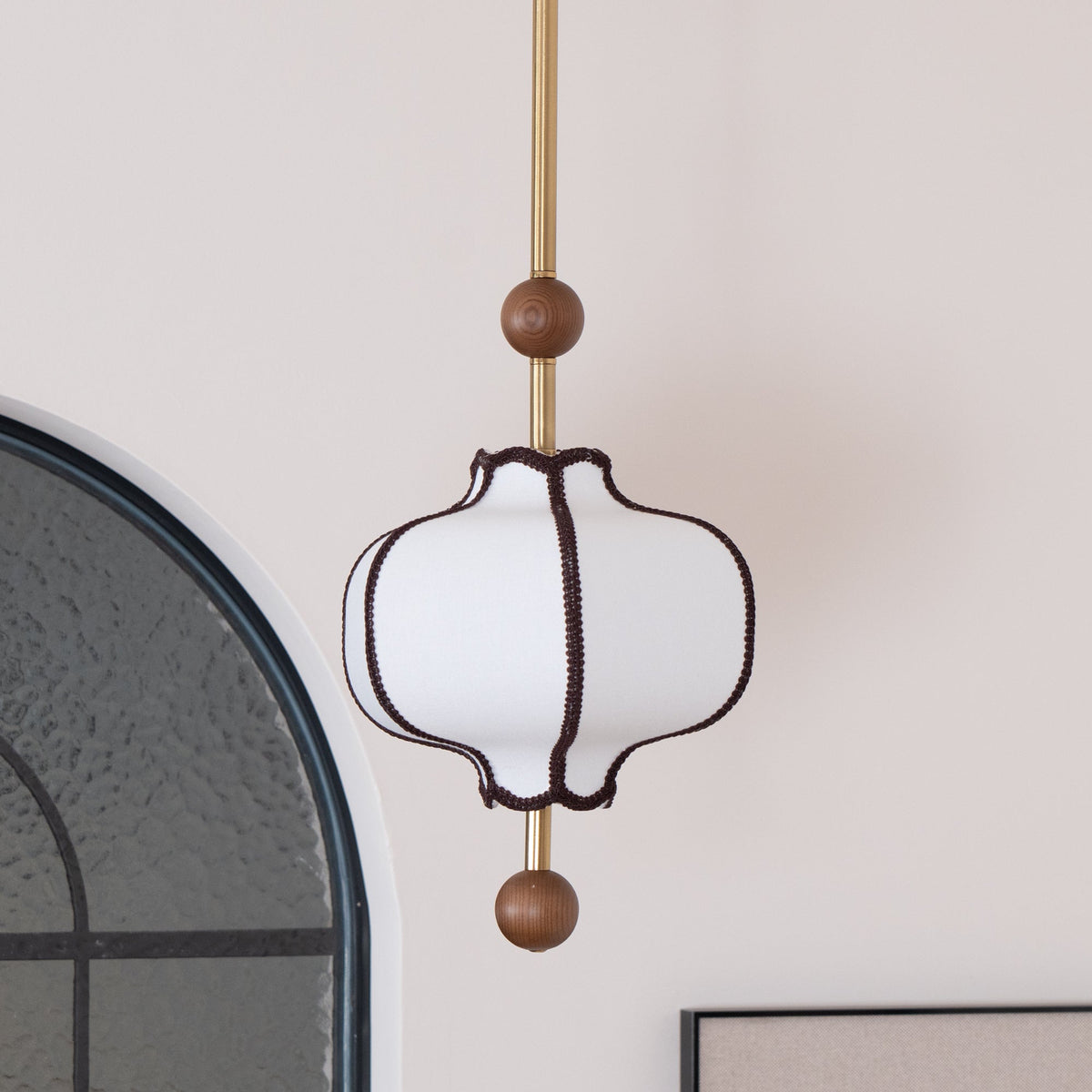 Unlit white lantern pendant with brown braid trim beside an arched black-framed mirror.