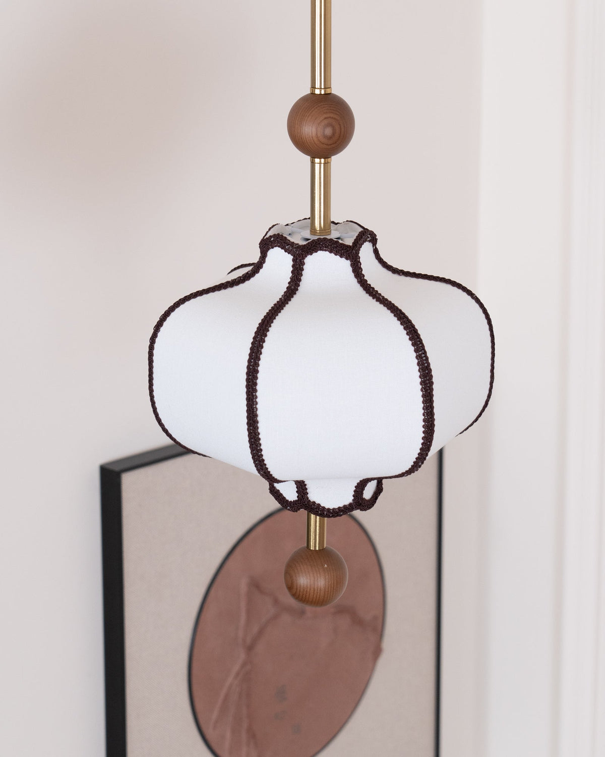 Close view from below of an unlit white lantern shade, its scalloped hem edged in brown braid.