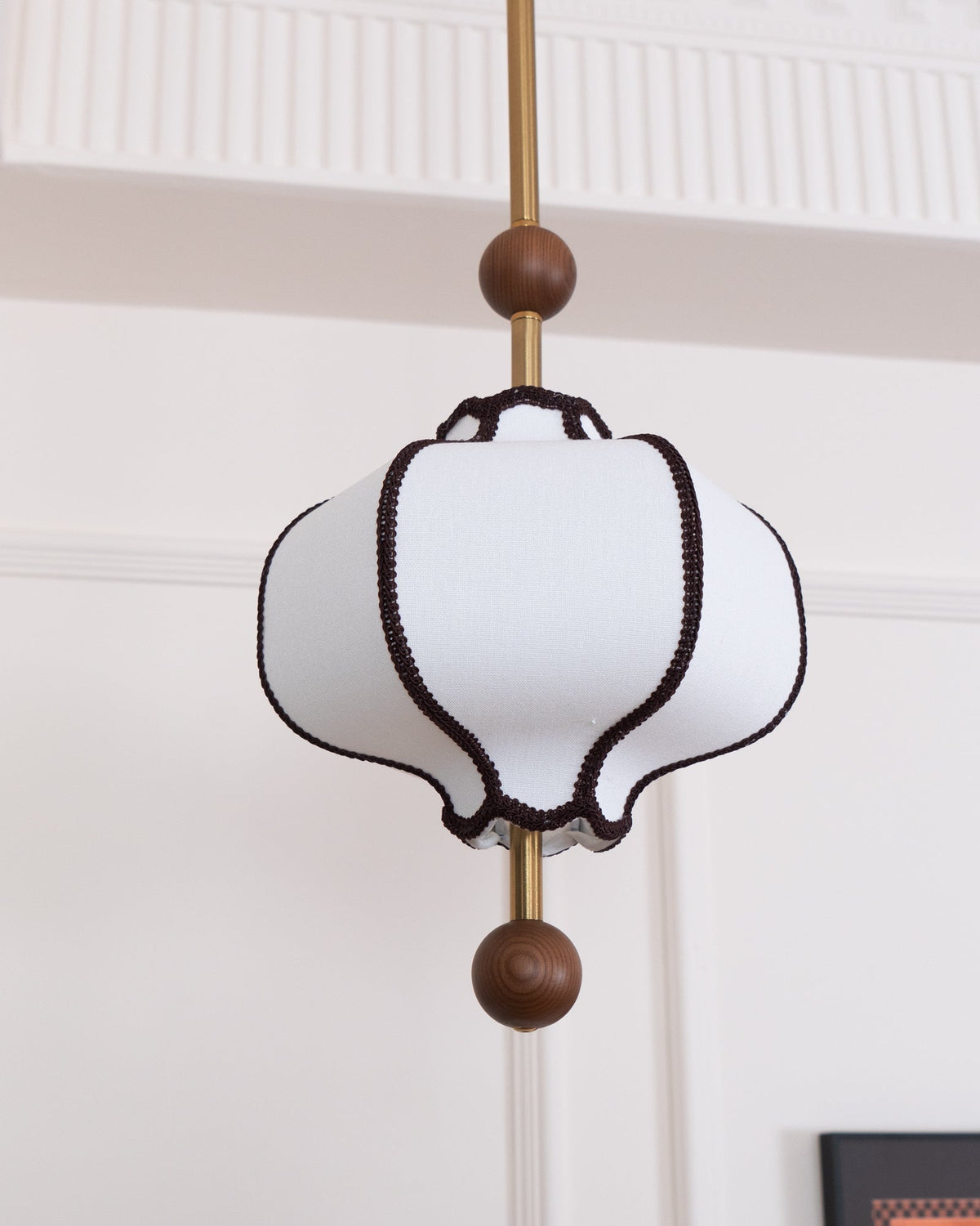 Unlit white fabric lantern shade with brown braid trim below a fluted white cornice.
