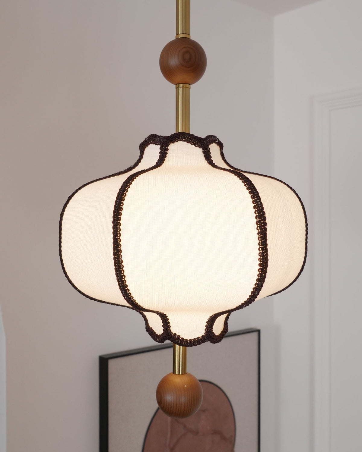Lit white fabric lantern shade seen from below, its scalloped hem edged in brown braid.