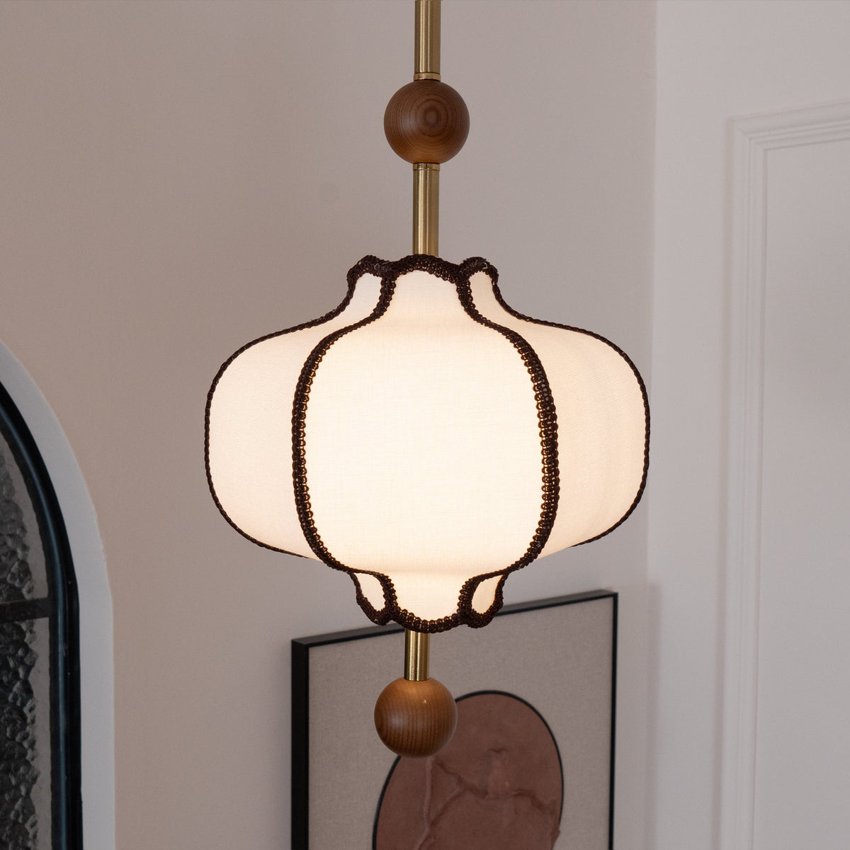 Lit white lantern pendant on a brass rod beside an arched mirror in a plain white room.