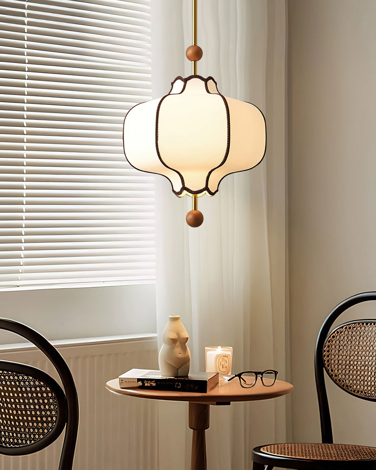 Lit white lantern pendant above a small round table between two black bentwood cane chairs.