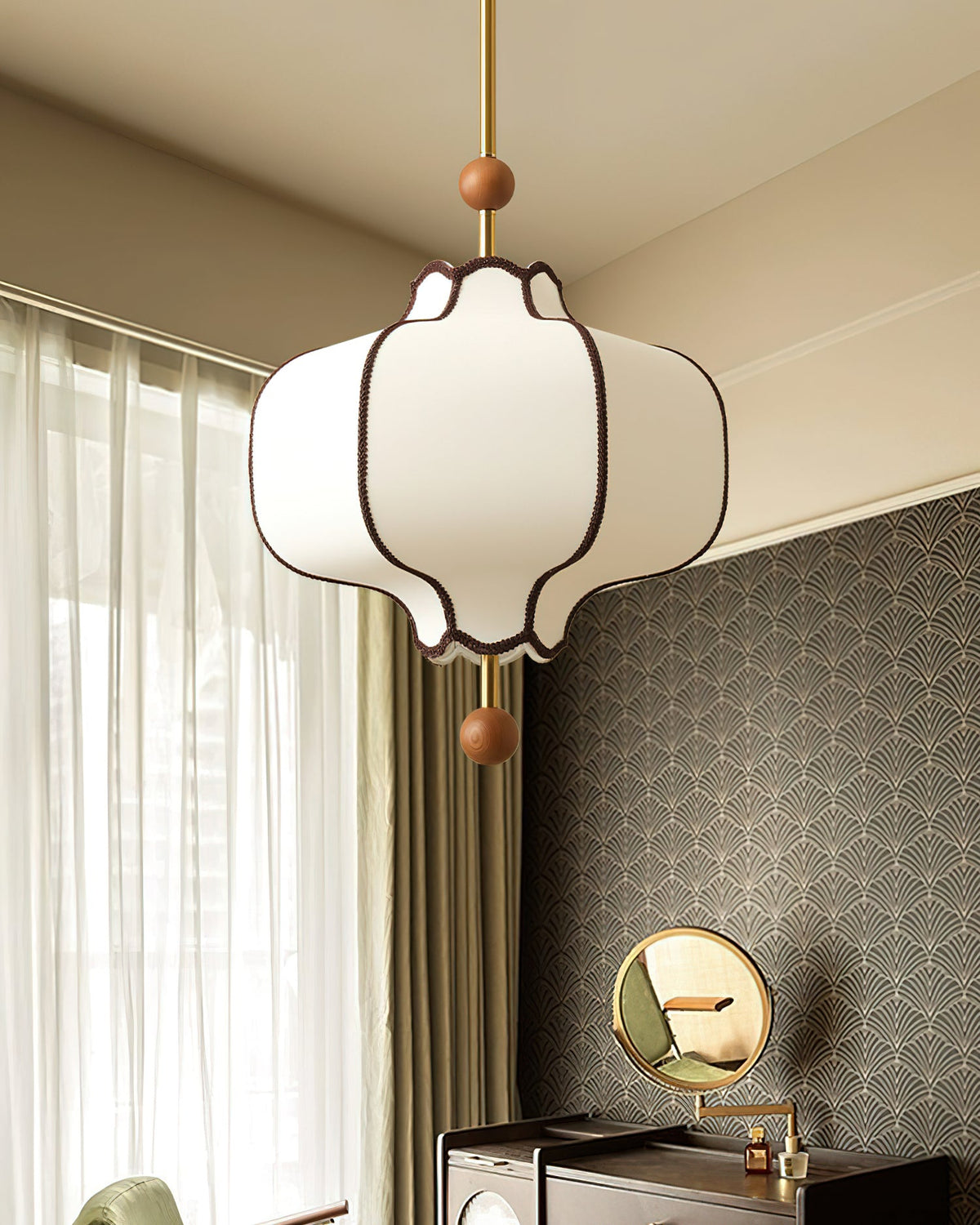 Lit white lantern pendant beside fan-pattern wallpaper and a round brass dressing mirror.