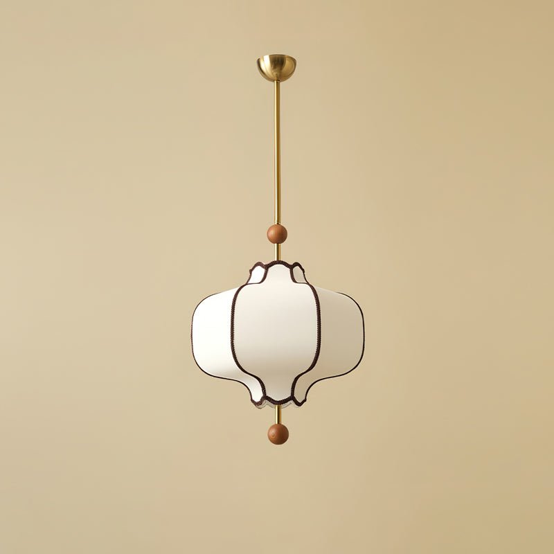 White fabric lantern pendant with brown braid trim on a brass rod, unlit, on a beige ground.