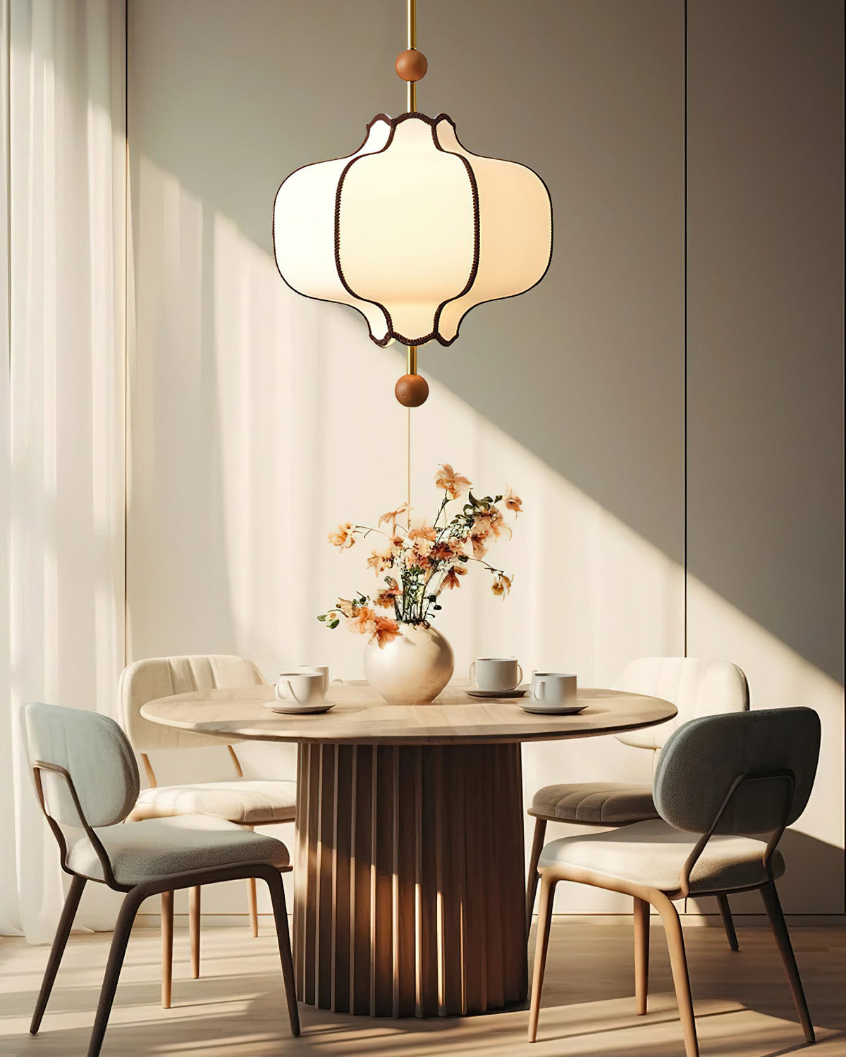 Lit white lantern pendant above a round pedestal dining table set with cups and dried flowers.