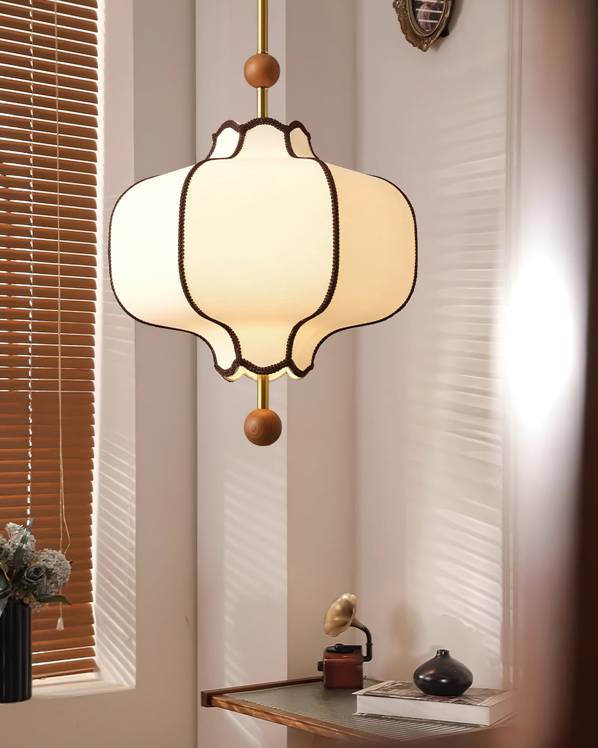 Lit white fabric lantern pendant in a corner with wooden venetian blinds and a small desk.
