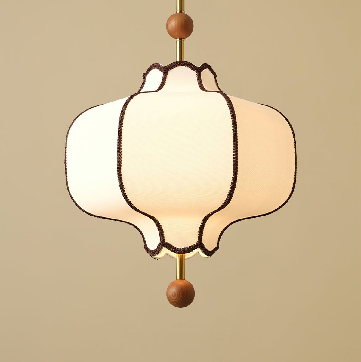 Close view of a lit white fabric lantern shade edged in brown braid, on an olive ground.