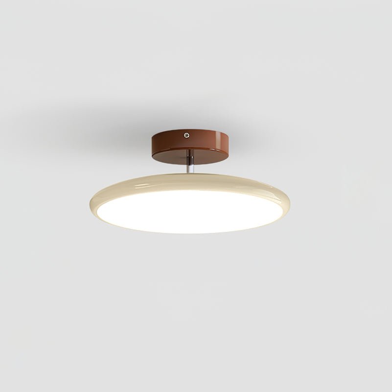 Drift flush-mount ceiling lamp with a shallow cream domed shade lit from within, on a slim stem below a rust-red canopy, against a plain pale ceiling.