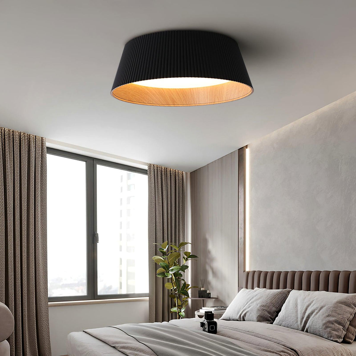 Drum-shaped flush ceiling light with a ribbed black outer, a wood-look inner rim and a white diffuser fitted above a bed by a window.