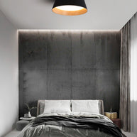 Drum-shaped flush ceiling light with a ribbed black outer, a wood-look inner rim and a white diffuser fitted above a bed against a textured wall.