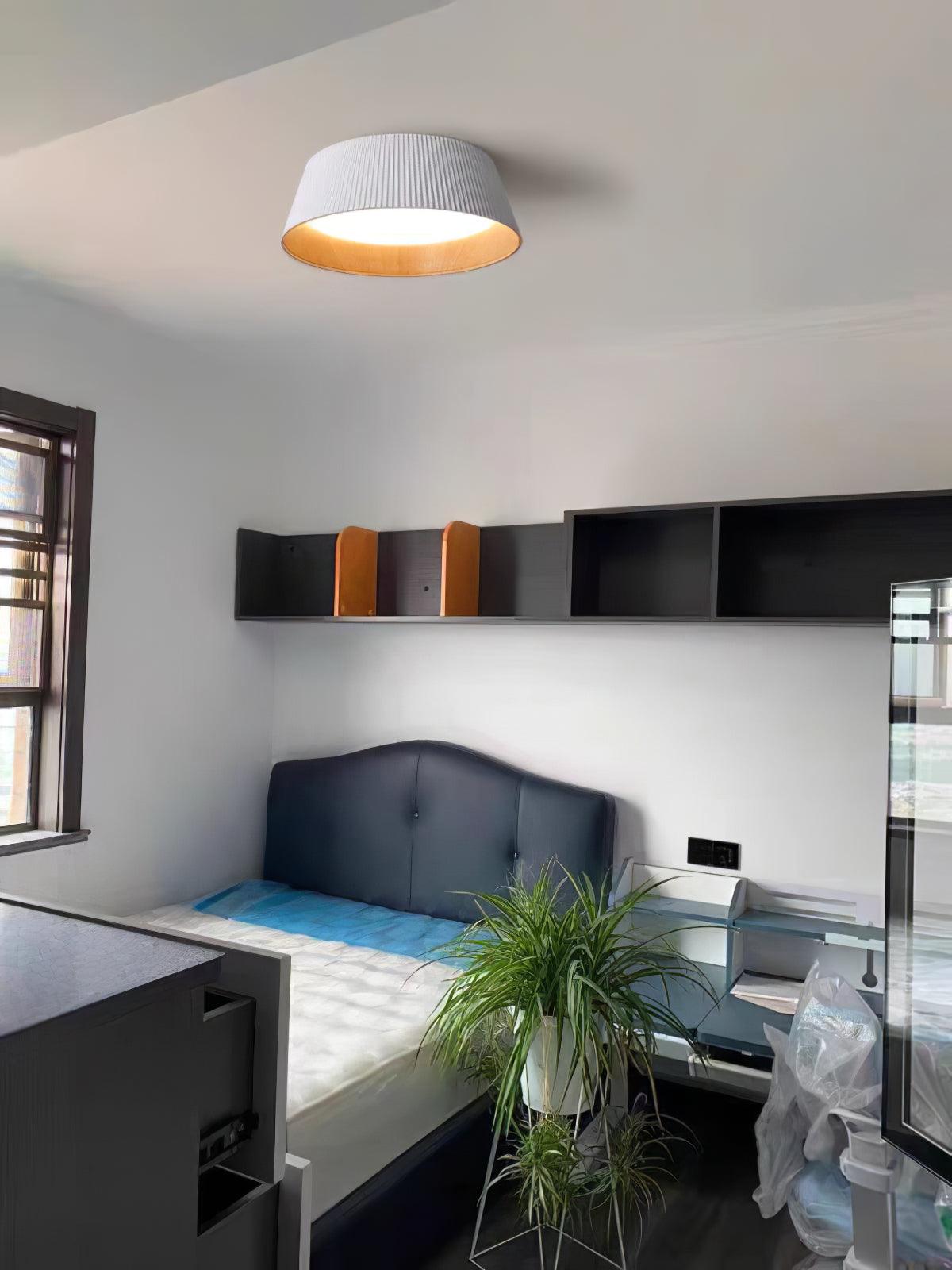 Drum-shaped flush ceiling light with a ribbed white outer, a wood-look inner rim and a white diffuser fitted to a ceiling above a desk and shelves.