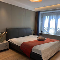 Drum-shaped flush ceiling light with a ribbed black outer, a wood-look inner rim and a white diffuser fitted above a bed with a red throw.