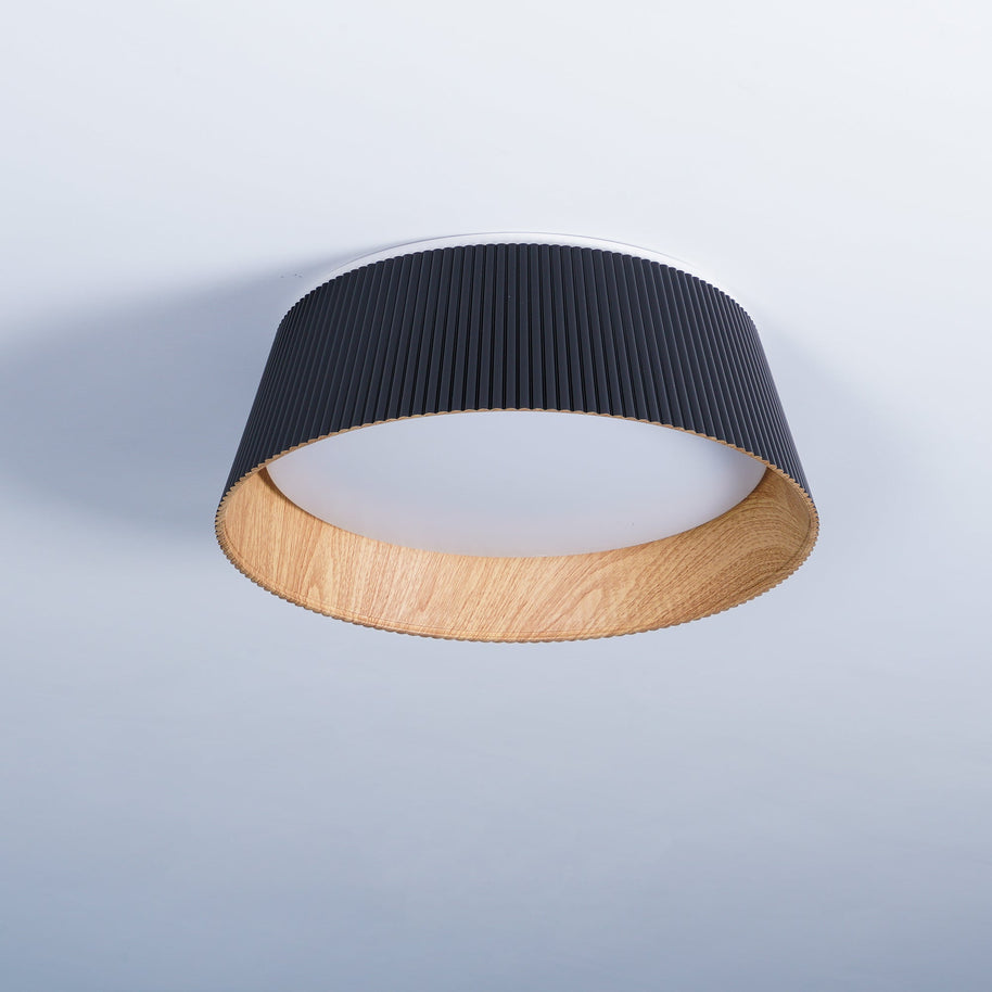 Drum-shaped flush ceiling light with a ribbed black outer, a wood-look inner rim and a white diffuser, seen at an angle on a plain background.
