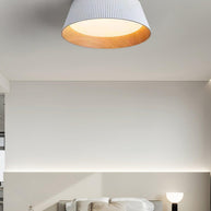 Drum-shaped flush ceiling light with a ribbed white outer, a wood-look inner rim and a white diffuser fitted to a ceiling above a bed.