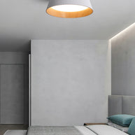 Drum-shaped flush ceiling light with a ribbed white outer, a wood-look inner rim and a white diffuser fitted to a ceiling in a bedroom with a concrete wall.