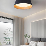 Drum-shaped flush ceiling light with a ribbed black outer, a wood-look inner rim and a white diffuser fitted above a bed by a full-height window.