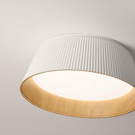 Drum-shaped flush ceiling light with a ribbed white outer, a wood-look inner rim and a white diffuser, seen from below at an angle.