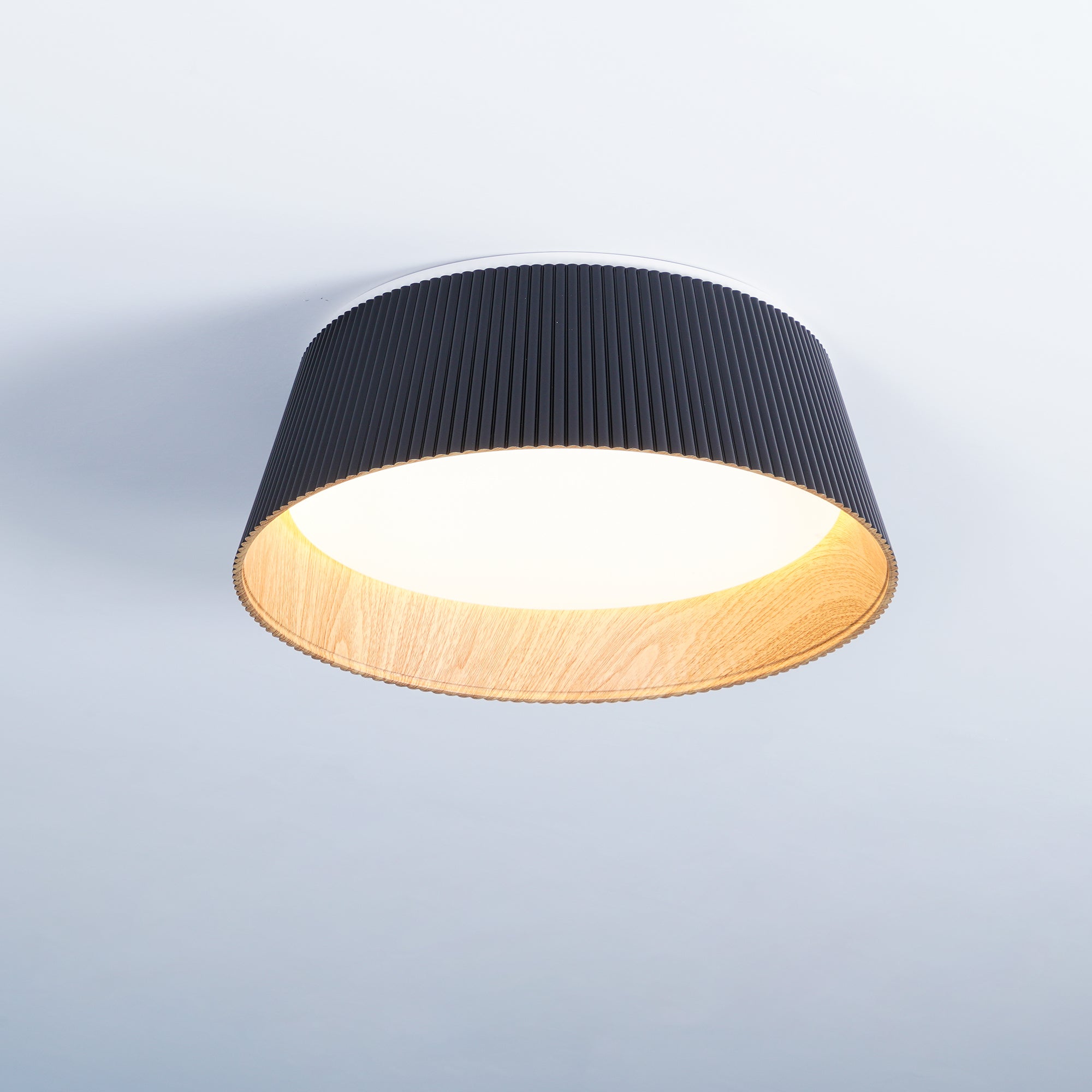 Drum-shaped flush ceiling light with a ribbed black outer, a wood-look inner rim and a white diffuser fitted to a ceiling.