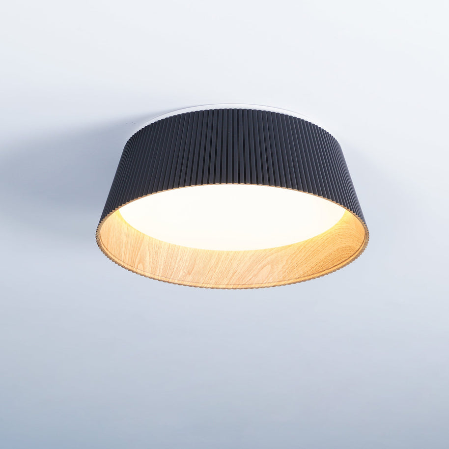 Drum-shaped flush ceiling light with a ribbed black outer, a wood-look inner rim and a white diffuser fitted to a ceiling.