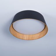 Drum-shaped flush ceiling light with a ribbed black outer, a wood-look inner rim and a white diffuser, seen from below at an angle.