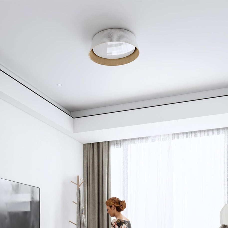 Drum-shaped flush ceiling light with a ribbed white outer, a wood-look inner rim and a white diffuser fitted to a ceiling in a room with a large window.