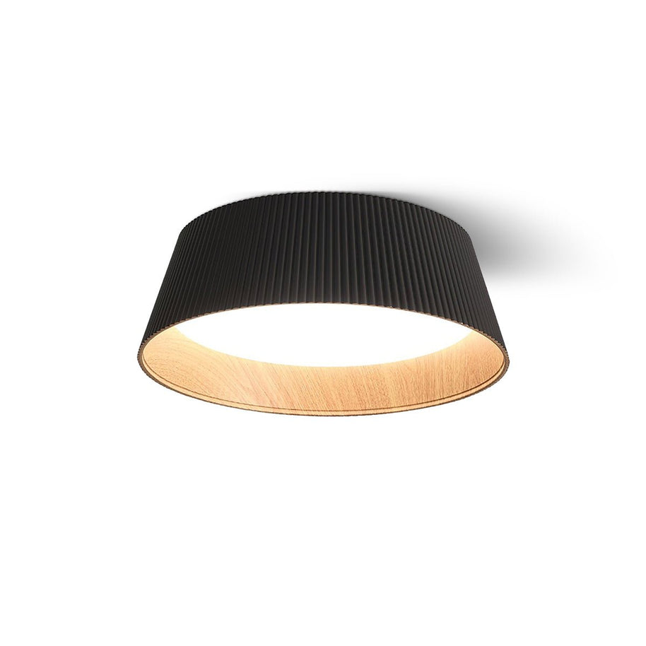 Drum-shaped flush ceiling light with a ribbed black outer, a wood-look inner rim and a white diffuser, lit, on a white background.