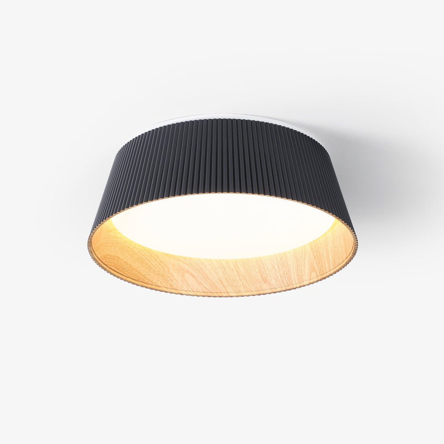 Drum-shaped flush ceiling light with a ribbed black outer, a wood-look inner rim and a white diffuser, seen at an angle on a plain background.