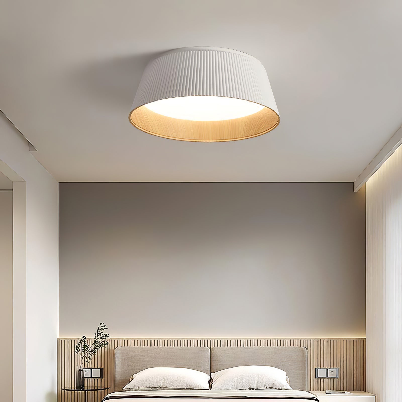Drum-shaped flush ceiling light with a ribbed white outer, a wood-look inner rim and a white diffuser fitted above a bed.