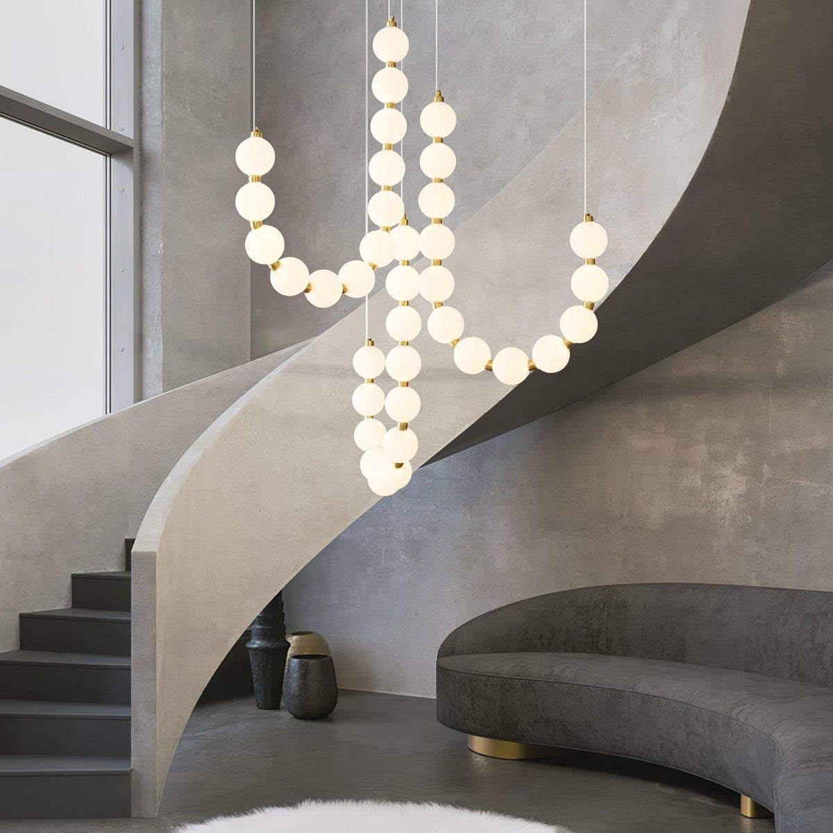 Perloria Chandelier, looping strands of lit opal globes beside a concrete spiral staircase