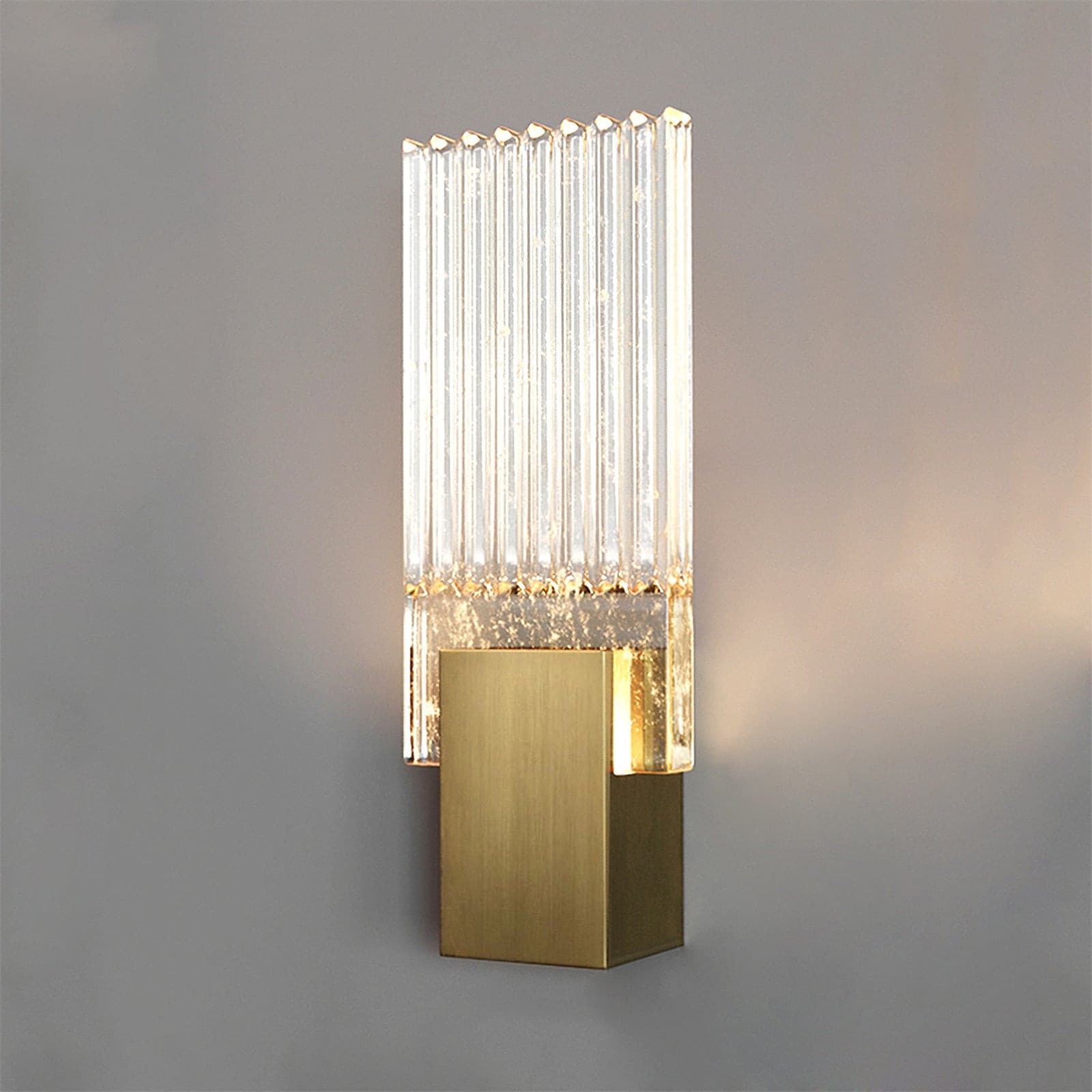 Wall light with a ribbed clear glass panel and a brushed brass mount lit against a grey wall.